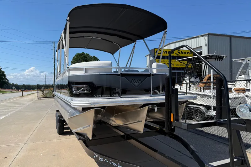 Slide: The Image of 2026 Avalon Venture 85 Versatile rear Bench pontoon boat on trailer, parked outdoors. - 2