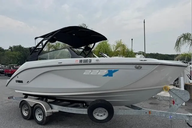 The Image of 2023 Yamaha Boats 222XD on trailer, sleek design, white exterior, black canopy, parked outdoors. - 0