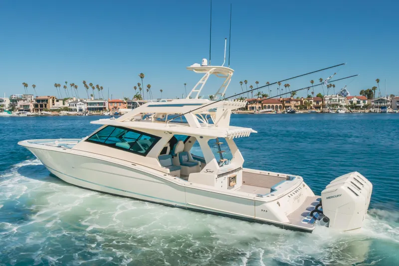 Slide: The Image of 2023 Scout 530 LXF luxury boat cruising on a sunny day near coastal homes. - 32