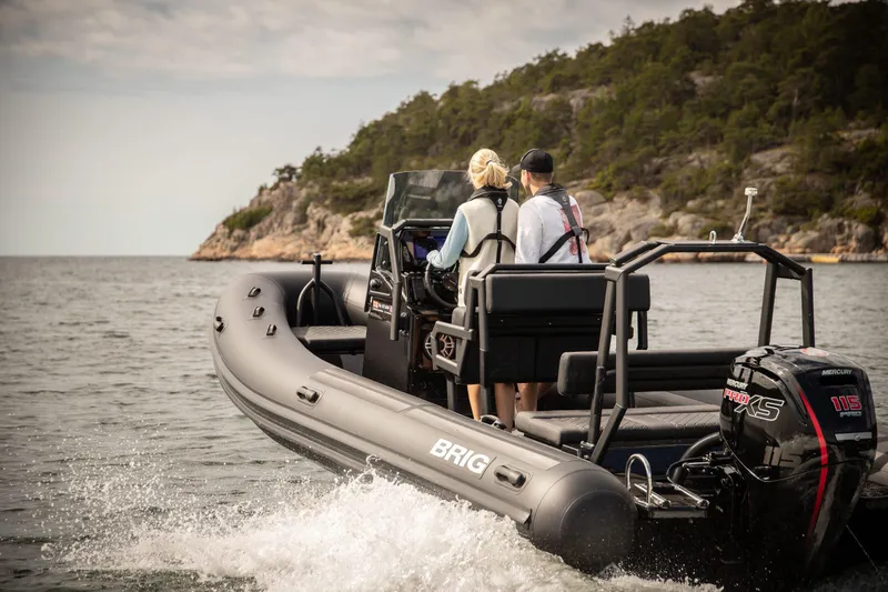Slide: The Image of 2026 Brig Navigator 20 boat cruising near rocky shoreline with two passengers. - 5