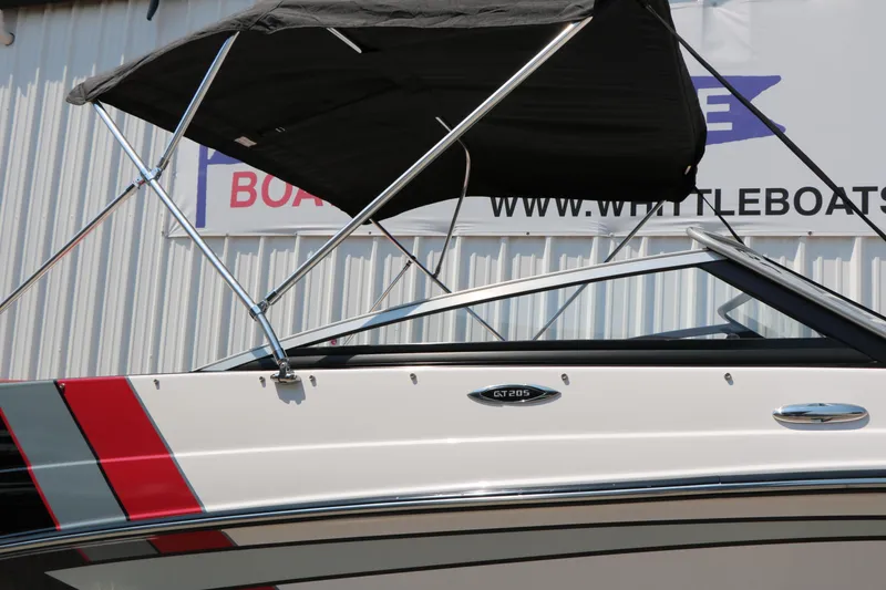 Slide: The Image of 2015 Glastron 205 GTS boat with canopy, side view, near Whittle Boats sign. - 12