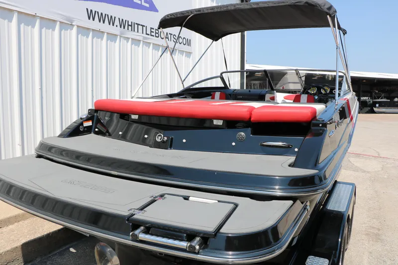Slide: The Image of 2015 Glastron 205 GTS boat with red seating and canopy, docked near a warehouse. - 4