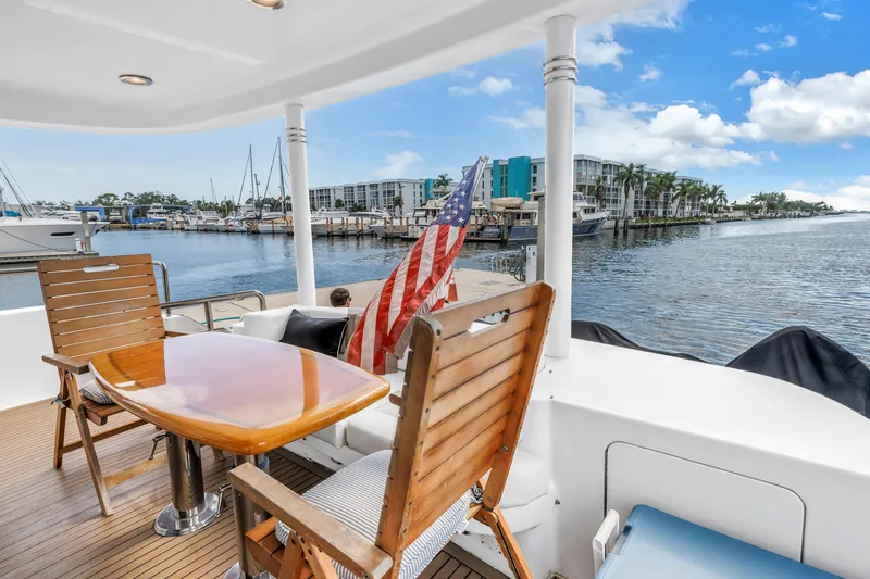 Slide: The Image of Luxury Neptunus 65 Flybridge yacht deck with wooden chairs, table, and marina view. - 19