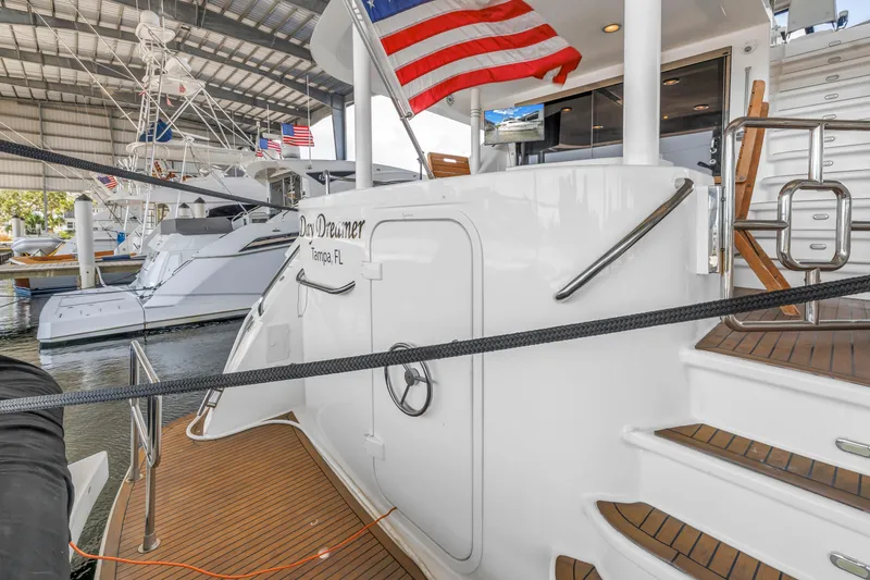 Slide: The Image of 2000 Neptunus 65 Flybridge yacht docked, featuring American flag and elegant wooden deck. - 23