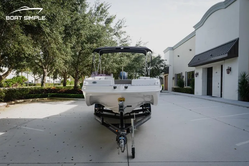 Slide: The Image of 2023 Starcraft SVX 211 OB boat on trailer, parked in a driveway with trees and buildings. - 6