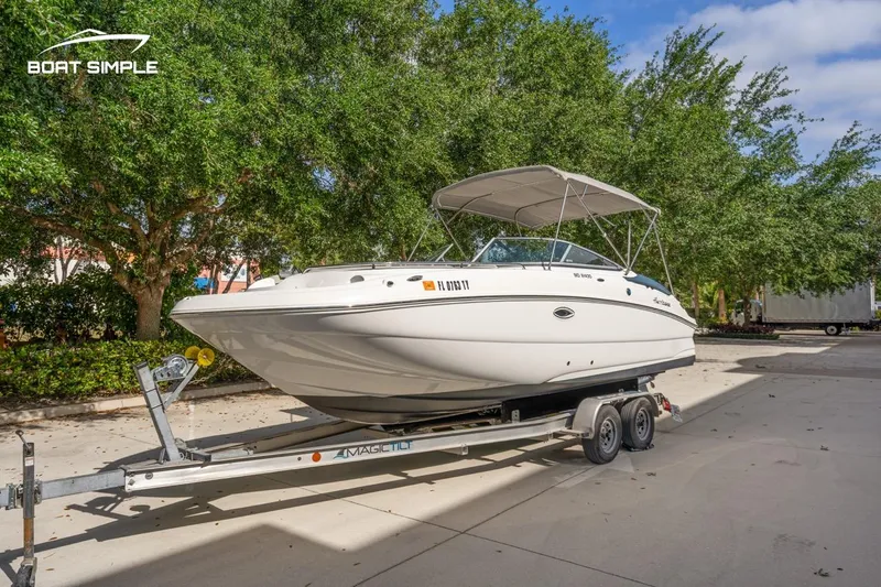 Slide: The Image of 2025 Hurricane SunDeck 2400 OB boat on trailer, parked outdoors with trees in background. - 2