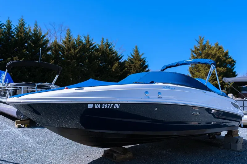 Slide: The Image of 2013 Sea Ray 240 Sundancer boat on display, covered, with trees in the background. - 0