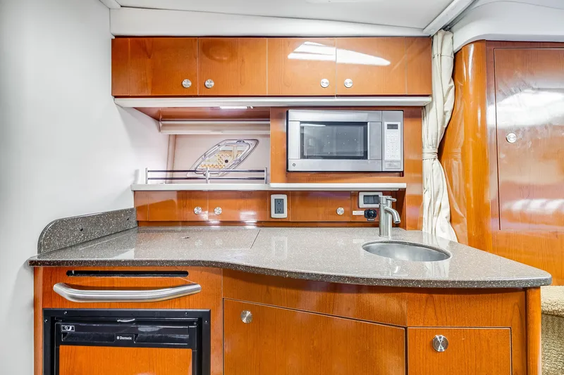 Slide: The Image of 2014 Sea Ray 330 Sundancer galley with microwave, sink, and wooden cabinetry. - 12