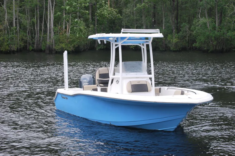Slide: The Image of 2021 Tidewater 210 CC Adventure boat on a serene lake with forest backdrop. - 2