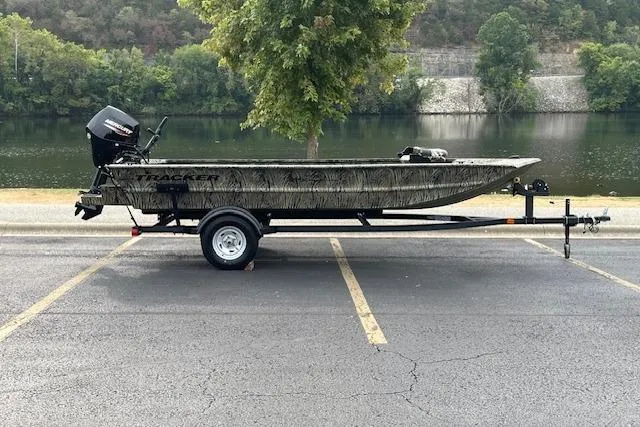The Image of 2026 Tracker Grizzly 1654 T Sportsman boat on trailer by scenic lake and autumn trees. - 0