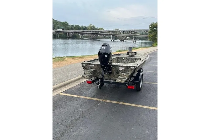 Slide: The Image of 2026 Tracker Grizzly 1654 T Sportsman boat on trailer, camo design, parked by a scenic river. - 5