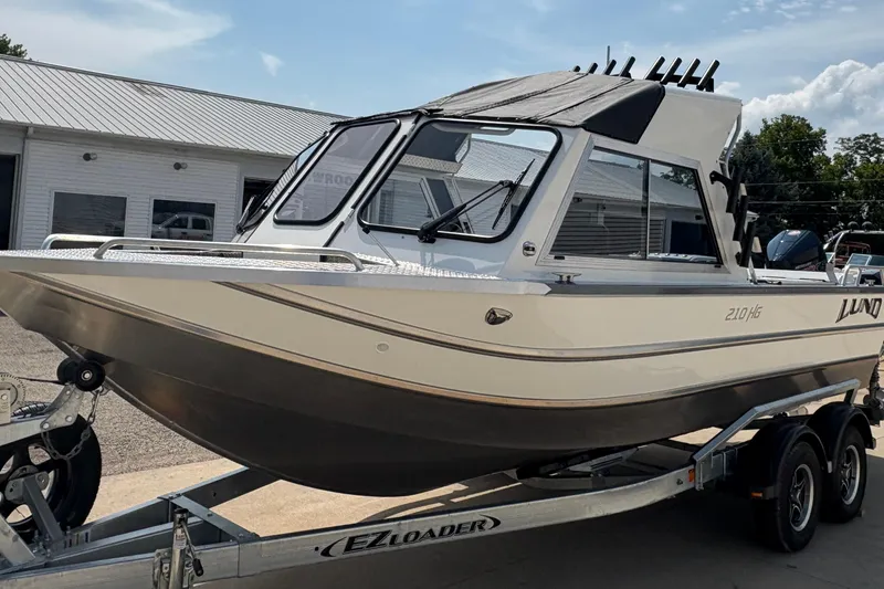 Slide: The Image of 2026 Lund 210 HG boat on trailer, parked outside a building under a clear sky. - 11