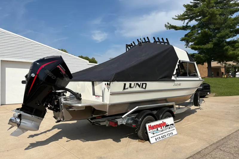 Slide: The Image of 2026 Lund 210 HG boat on trailer with cover, parked outdoors. - 12
