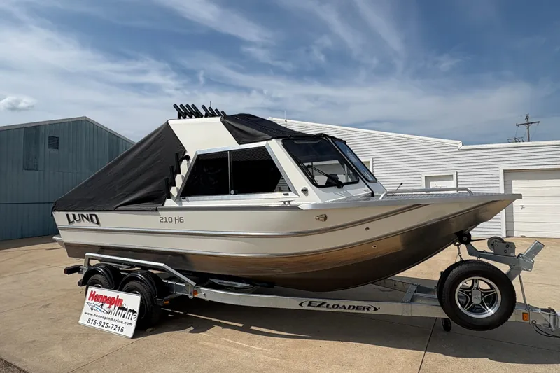 Slide: The Image of 2026 Lund 210 HG boat on trailer, covered, parked outside a building. - 14