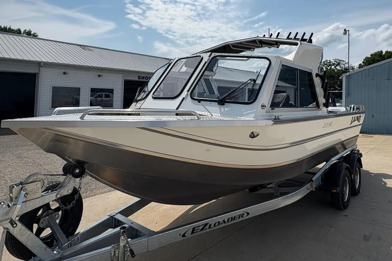 Slide: The Image of 2026 Lund 210 HG boat on trailer, parked outside a showroom under a partly cloudy sky. - 3