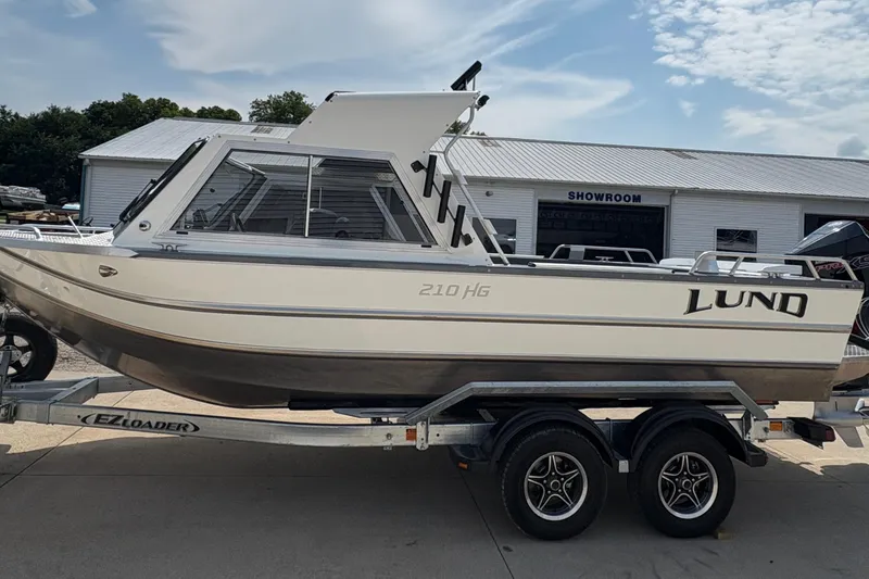 Slide: The Image of 2026 Lund 210 HG boat on trailer outside showroom under cloudy sky. - 4