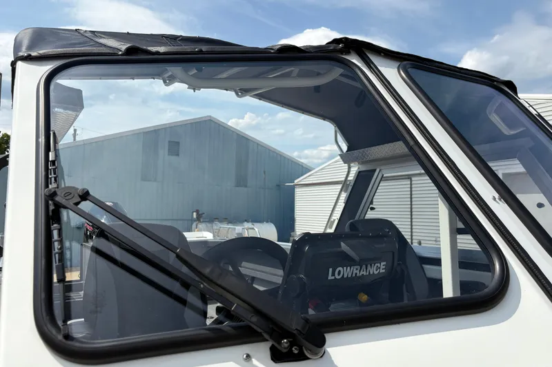 Slide: The Image of 2026 Lund 210 HG boat windshield with Lowrance equipment, parked near industrial buildings. - 51