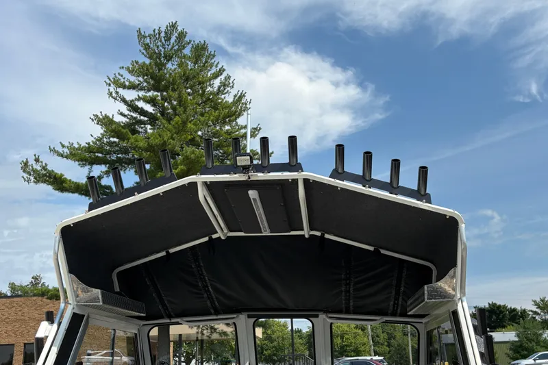 Slide: The Image of 2026 Lund 210 HG boat roof with rod holders under a clear blue sky. - 53