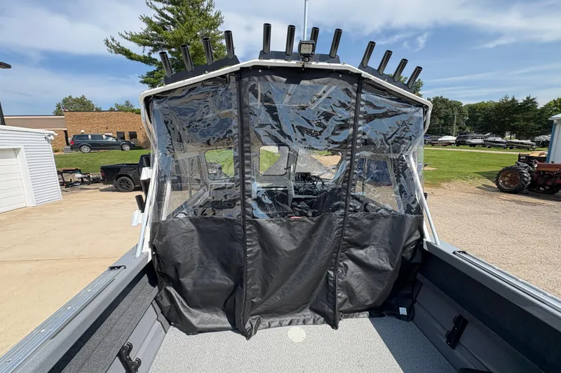 Slide: The Image of 2026 Lund 210 HG boat with clear protective cover and rod holders, parked outdoors. - 56