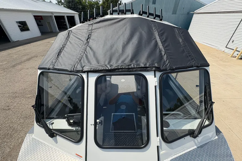 Slide: The Image of 2026 Lund 210 HG boat with black canopy and windshield, parked outside a building. - 8