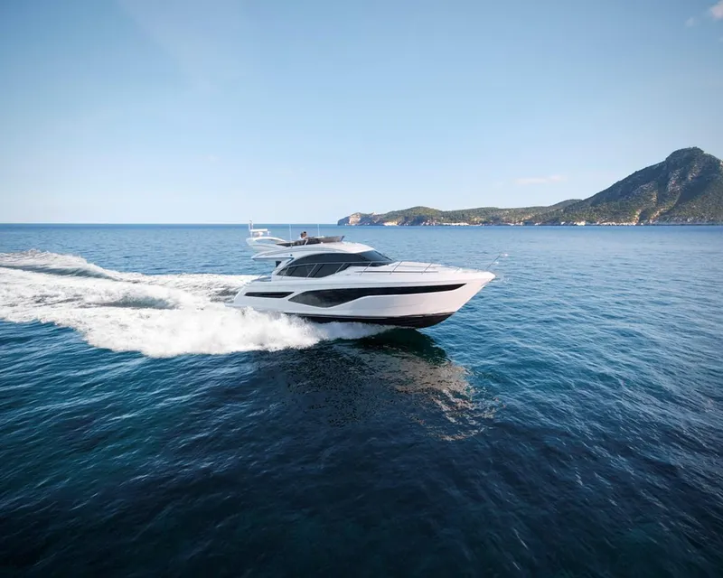 The Image of 2025 Princess 50 Flybridge yacht cruising on open sea with scenic island backdrop. - 0
