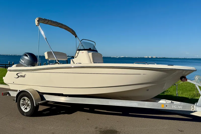 The Image of 2026 Scout 188 Sportfish boat on trailer by waterfront, clear blue sky. - 0