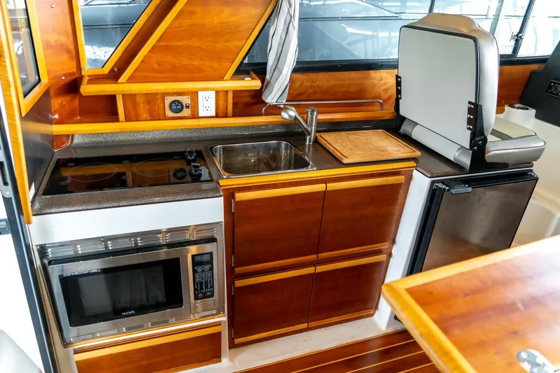 Slide: The Image of 2020 Cutwater C28 boat interior kitchen with wood cabinetry, sink, stove, microwave, and fridge. - 22