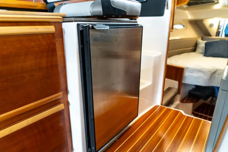 Slide: The Image of 2020 Cutwater C28 interior with wood cabinetry, compact fridge, and cozy sleeping area. - 25