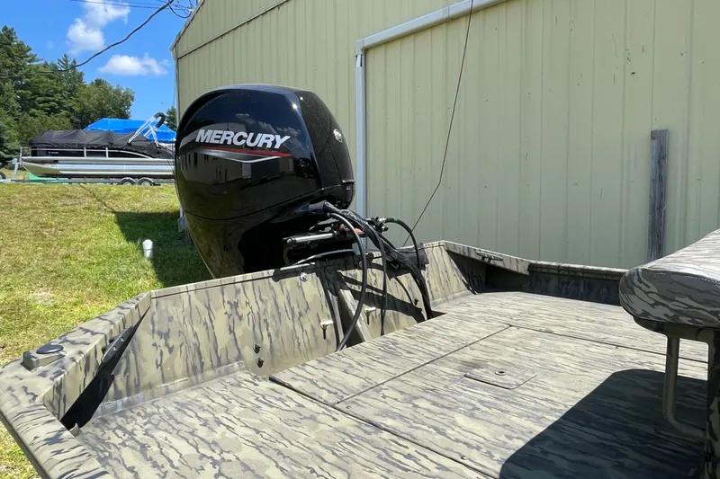 Slide: The Image of 2026 Lund 1870 Predator CC boat with Mercury engine, camo design, parked outdoors. - 3