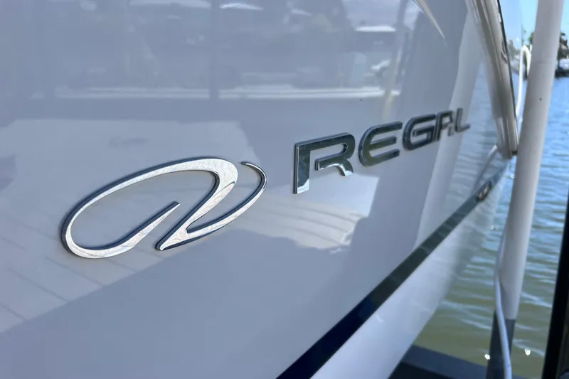 Slide: The Image of 2024 Regal 26 XO boat logo on sleek white hull by the water. - 3