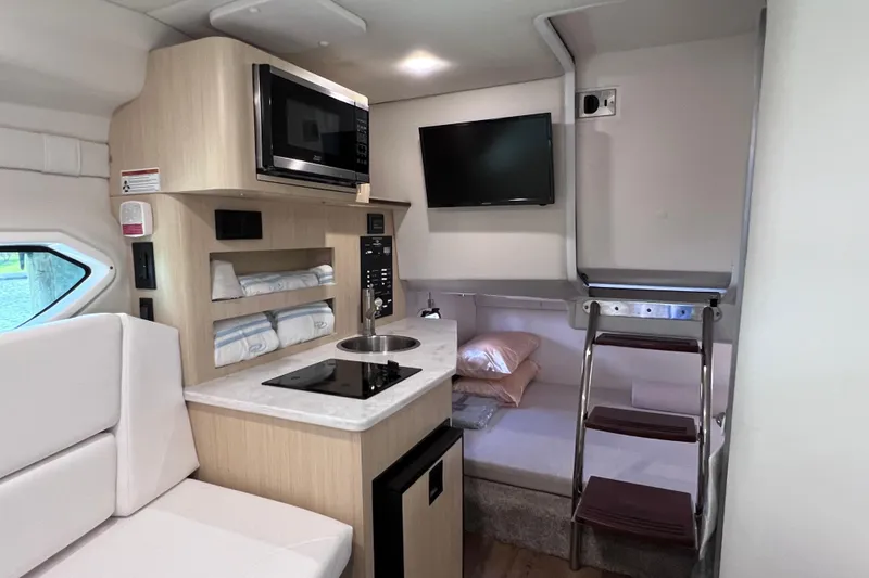 Slide: The Image of 2024 Regal 26 XO boat interior with kitchenette, microwave, TV, and cozy sleeping area. - 54