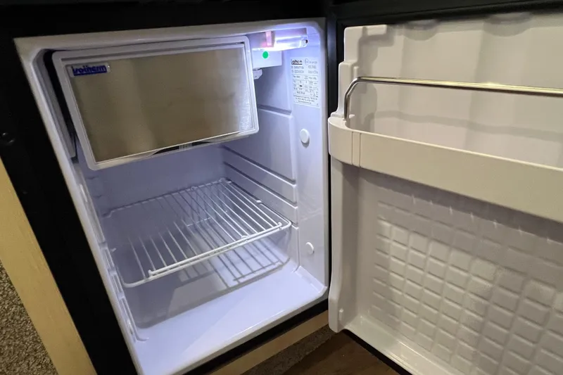 Slide: The Image of Open mini fridge inside 2024 Regal 26 XO boat, featuring wire shelf and door storage. - 55