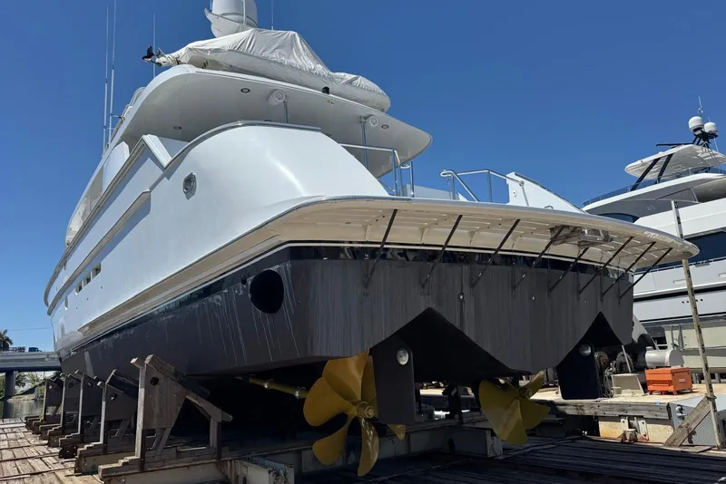 Slide: The Image of 2002 Hatteras 92 Cockpit Motor Yacht on dry dock, showcasing propellers and hull. - 55