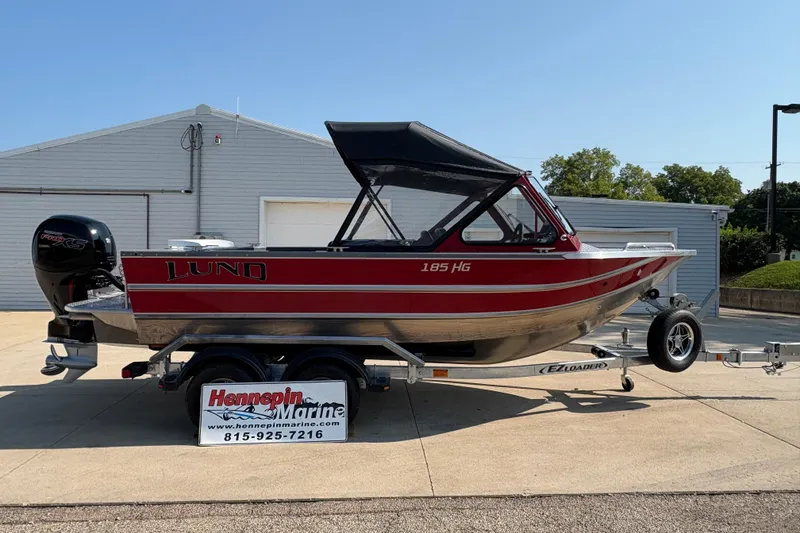 The Image of 2026 Lund 185 HG boat on trailer, red and silver, parked outside Hennepin Marine. - 0