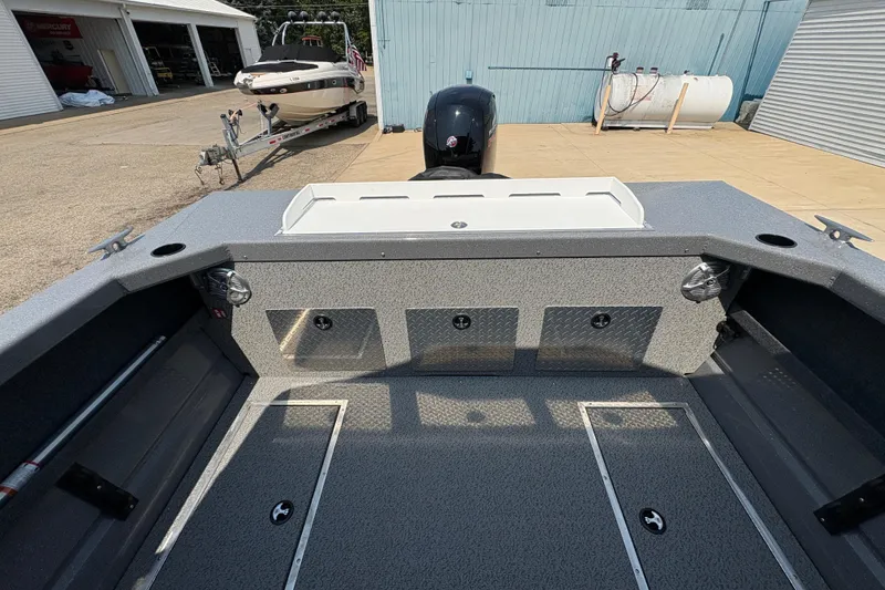 Slide: The Image of 2026 Lund 185 HG boat interior with storage compartments and motor, parked near a trailer. - 28