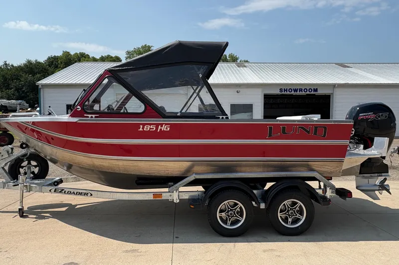 Slide: The Image of 2026 Lund 185 HG boat on trailer outside showroom, featuring red and silver design. - 5