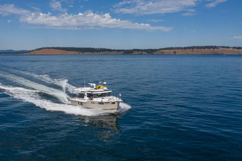 Slide: The Image of 2025 Ranger Tugs R-43 S cruising on a serene lake under a blue sky. - 2