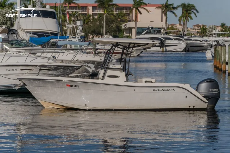 Slide: The Image of 2023 Cobia 220 Center Console boat docked in marina with palm trees. - 0