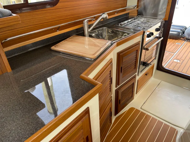 Slide: The Image of 2025 Ranger Tugs R-31S kitchen with wood cabinetry, stainless steel sink, and stove. - 28