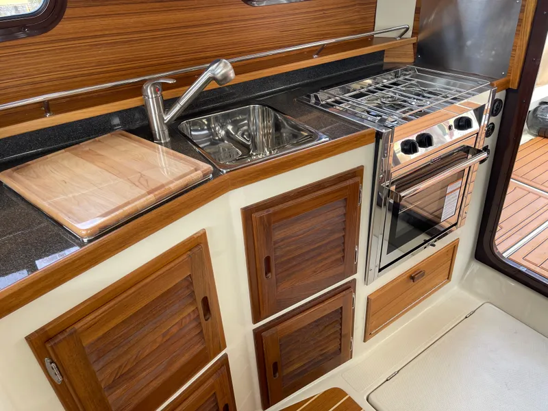 Slide: The Image of 2025 Ranger Tugs R-31S galley with stainless steel sink, stove, and wooden cabinetry. - 29