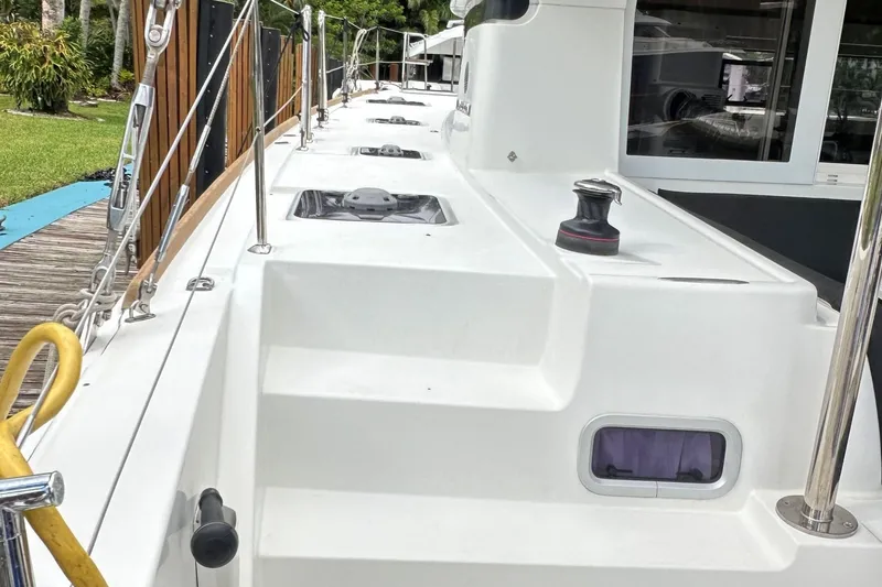 Slide: The Image of 2022 Lagoon 40 catamaran deck with winch and railing, docked near lush greenery. - 3