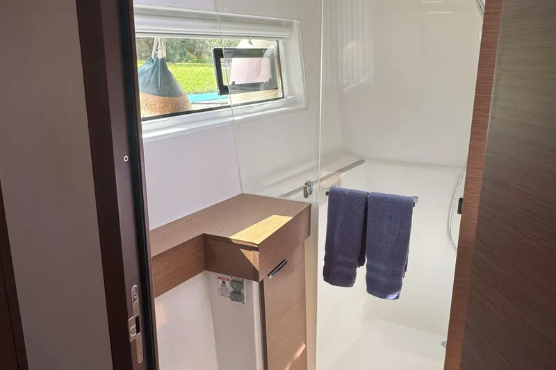 Slide: The Image of 2022 Lagoon 40 yacht bathroom with window, wooden accents, and blue towels. - 41