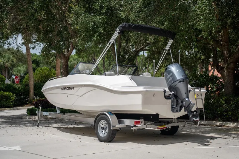 Slide: The Image of 2022 Starcraft SVX 190 DC boat on trailer, parked outdoors with trees in background. - 6