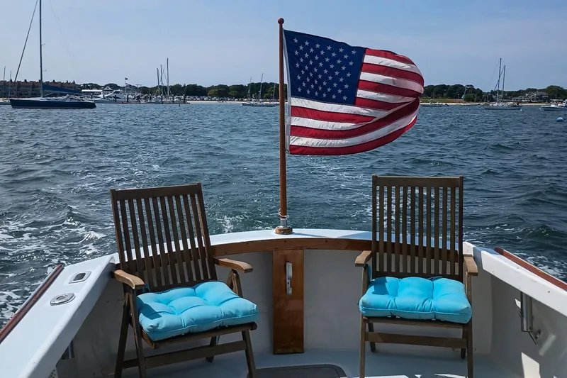 Slide: The Image of Dyer 29 boat with American flag, two chairs, and blue cushions on a sunny day. - 5