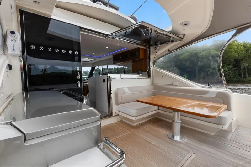 Slide: The Image of 2021 Riviera 5400 Sport Yacht Platinum Edition interior with seating and table, open water view. - 19