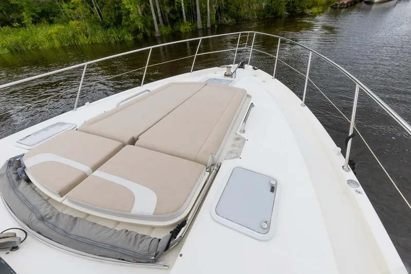 Slide: The Image of 2021 Riviera 5400 Sport Yacht Platinum Edition with sunbed on deck, near lush greenery. - 8