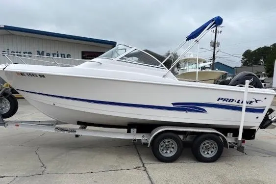 Slide: The Image of 2002 Pro-Line 20 DC boat on trailer, white with blue accents, parked outdoors. - 13