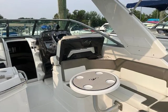 Slide: The Image of 2016 Monterey 275 Sport Yacht interior with helm, seating, and table in a marina setting. - 11