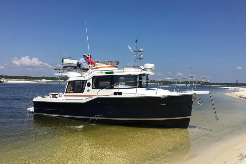 Slide: The Image of 2026 Ranger Tugs R-29 CB boat anchored on sandy shore under clear blue sky. - 16