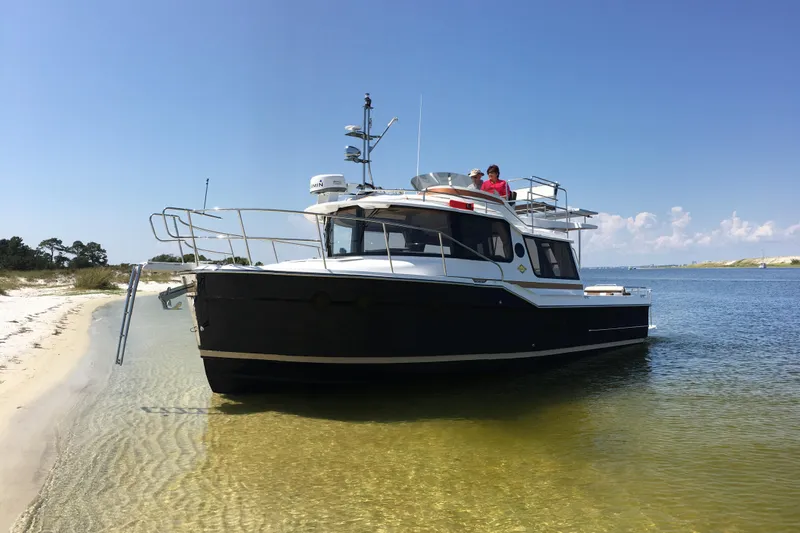 Slide: The Image of 2026 Ranger Tugs R-29 CB boat docked on a sandy beach under clear blue skies. - 17
